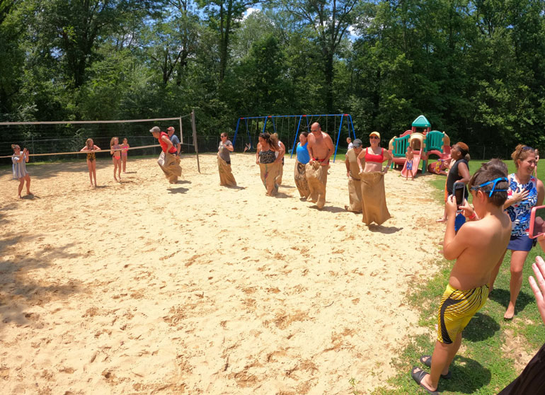 Children participating in a sack race in a sand pit at Fair Blue Swim Club
